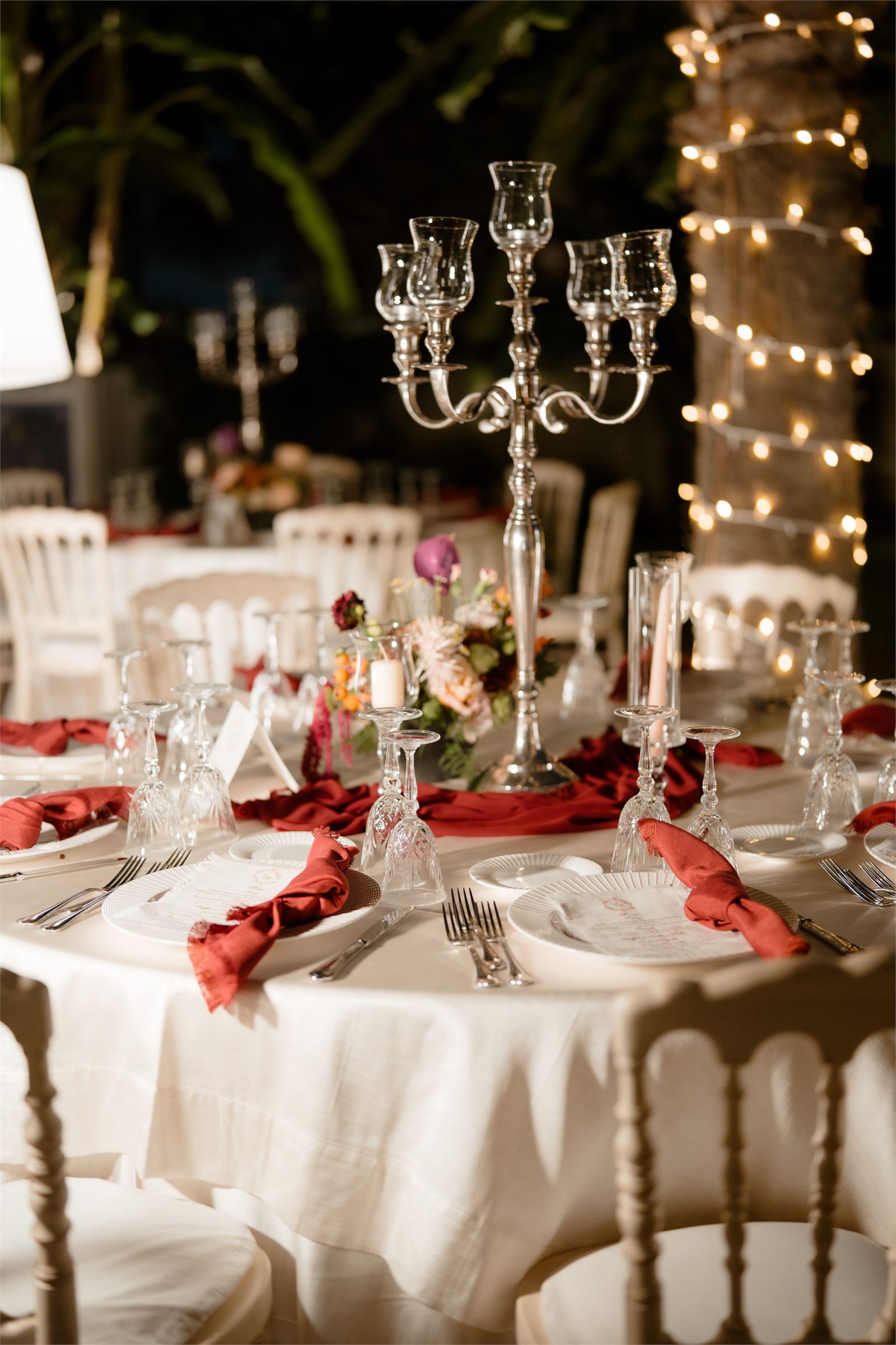 A candlelit outdoor reception table set with a silver candelabra, florals and string lights behind