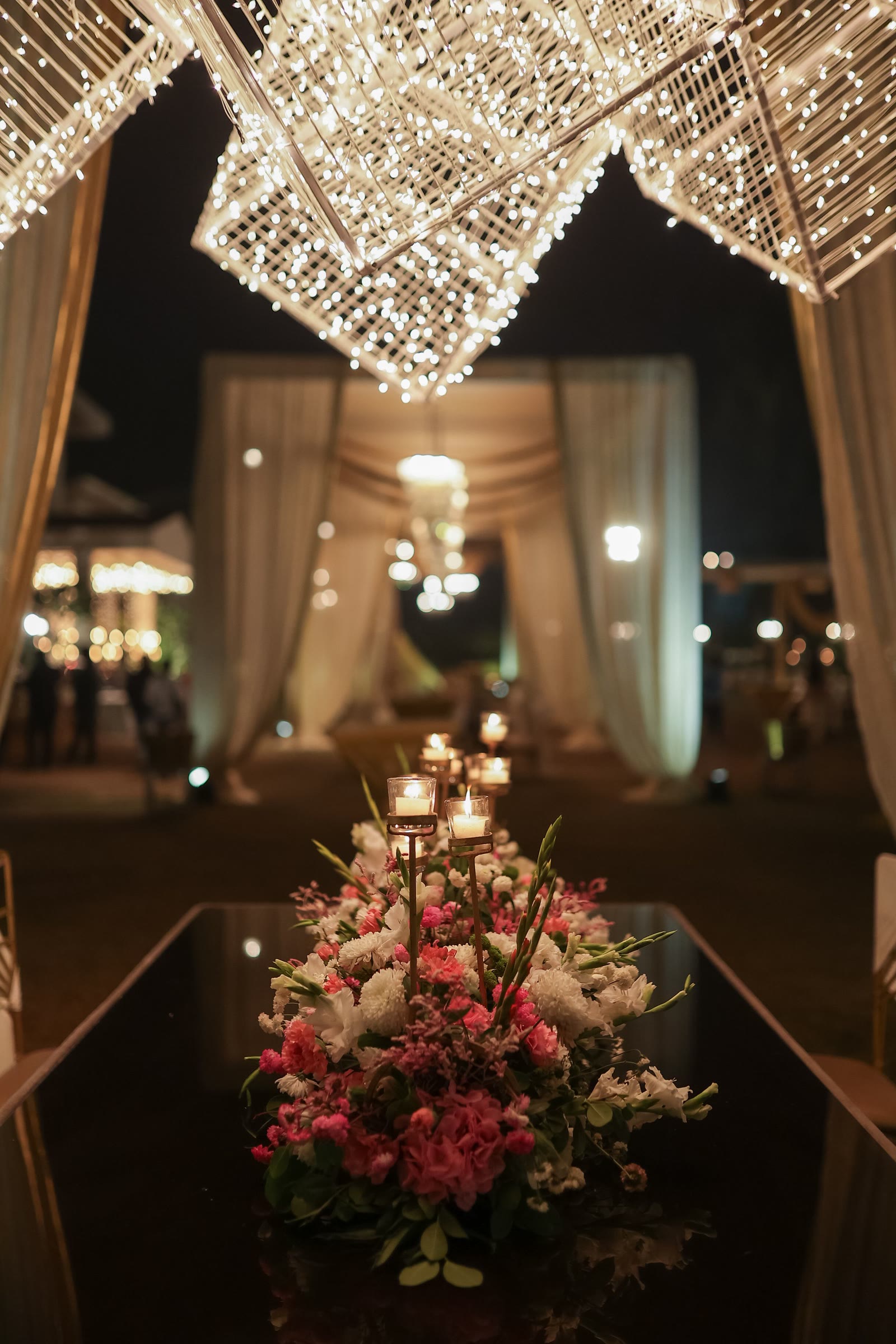 A candlelit banquet table dressed with flowers beneath a canopy of fairy lights