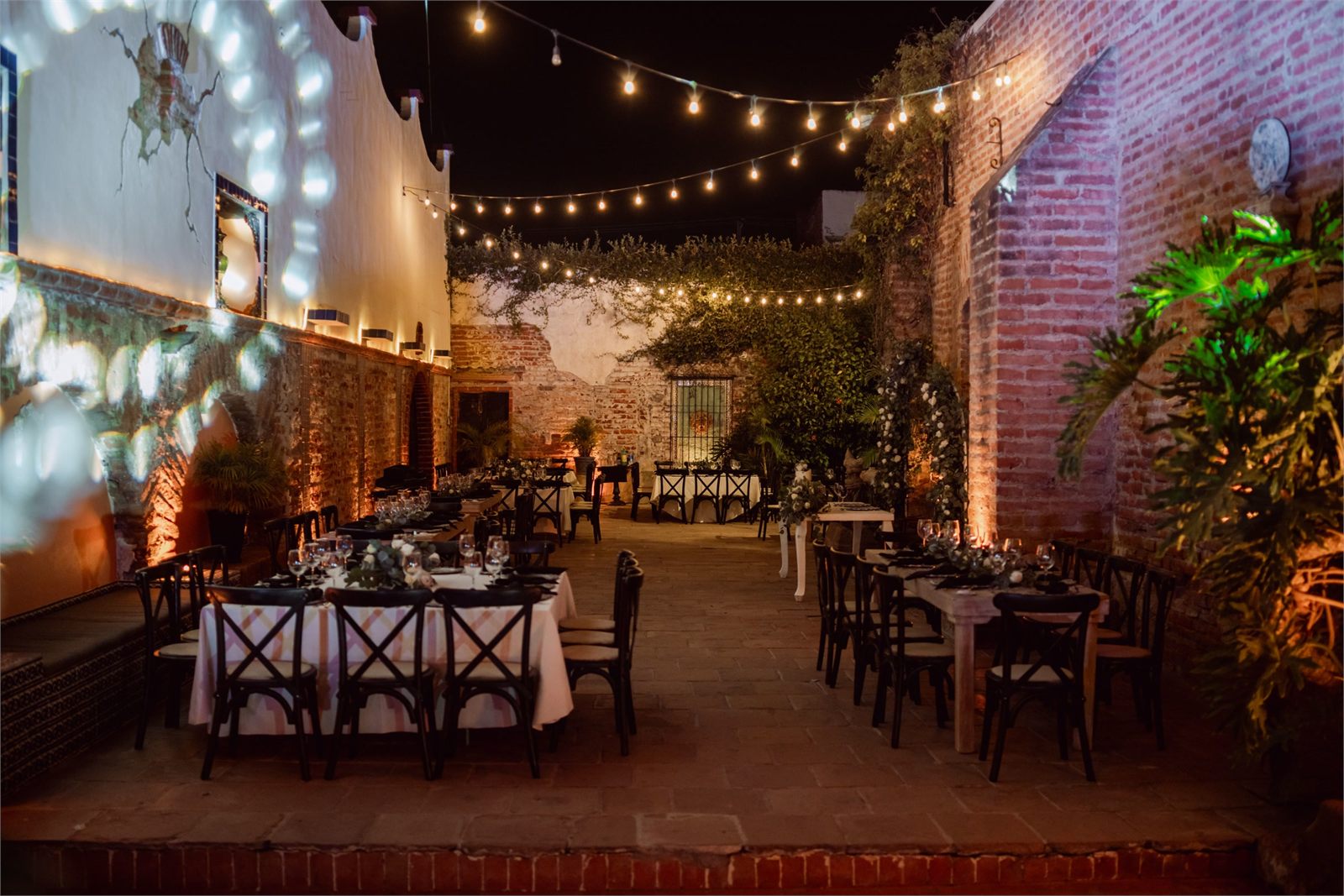 A courtyard of empty dressed tables under string lights after the guests have gone