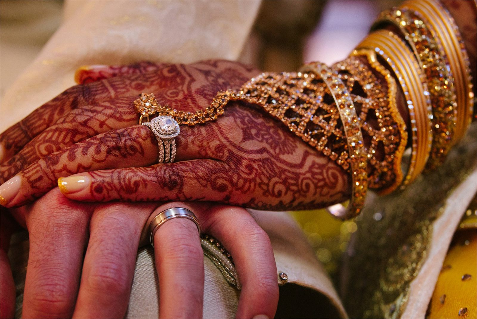 Hands patterned with henna resting together, gold bangles at the wrist