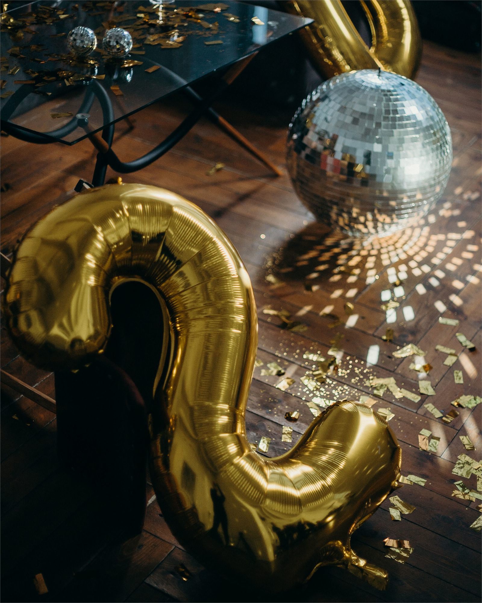 Gold foil balloons and a mirror ball scattering light across a dark wooden floor
