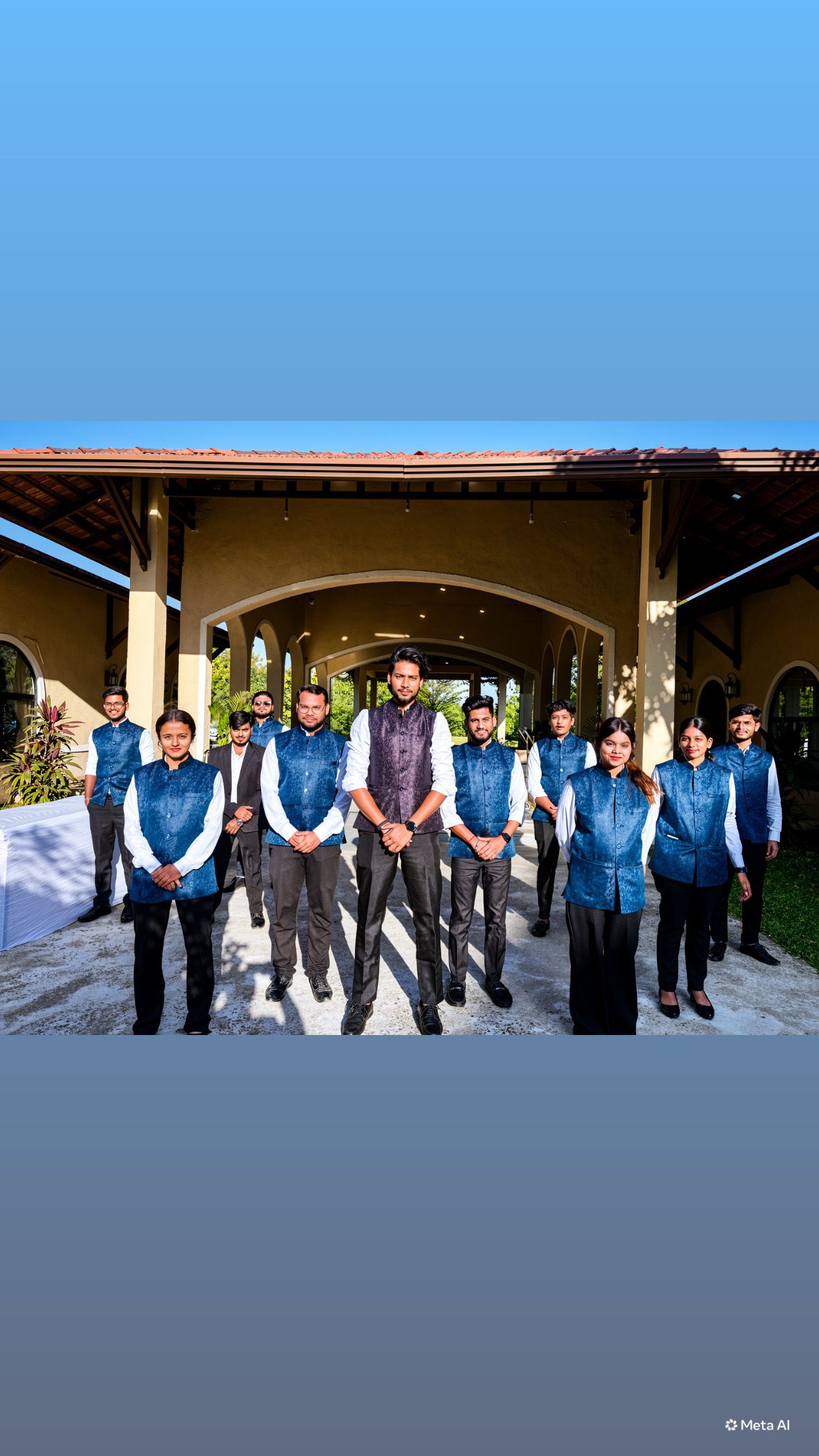 Indraa Events crew in blue nehru jackets standing under a tiled pavilion roof at a daytime function