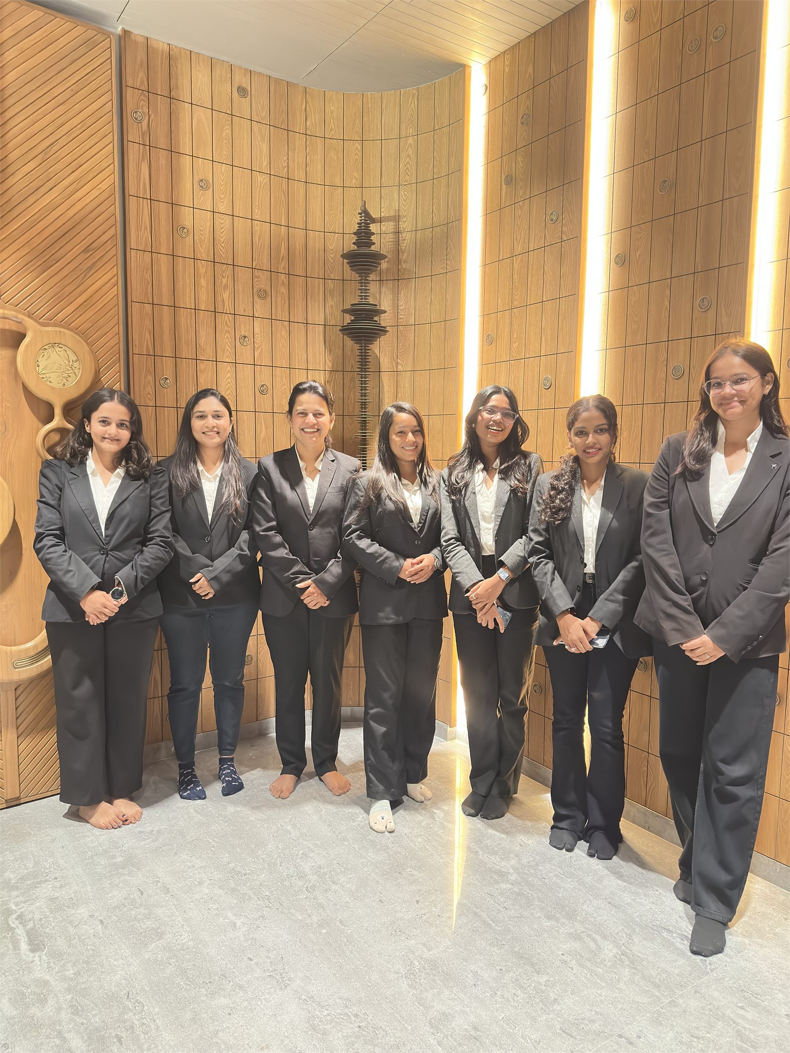Seven Indraa Events crew members in formal blazers in a wood-panelled corridor