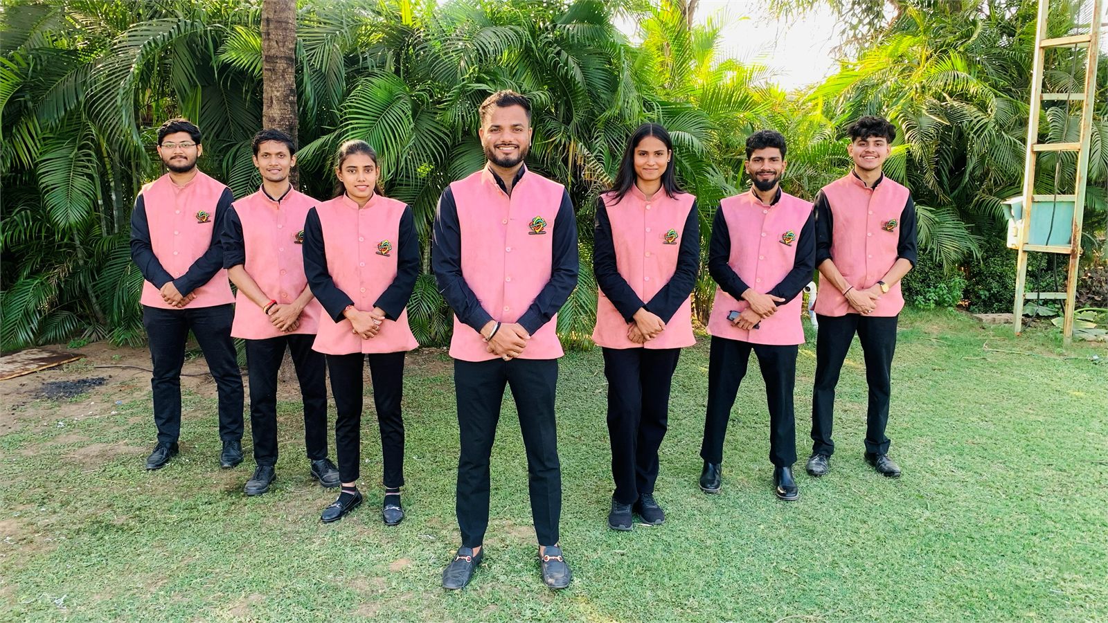 Seven Indraa Events crew members in pink and black nehru jackets on a lawn