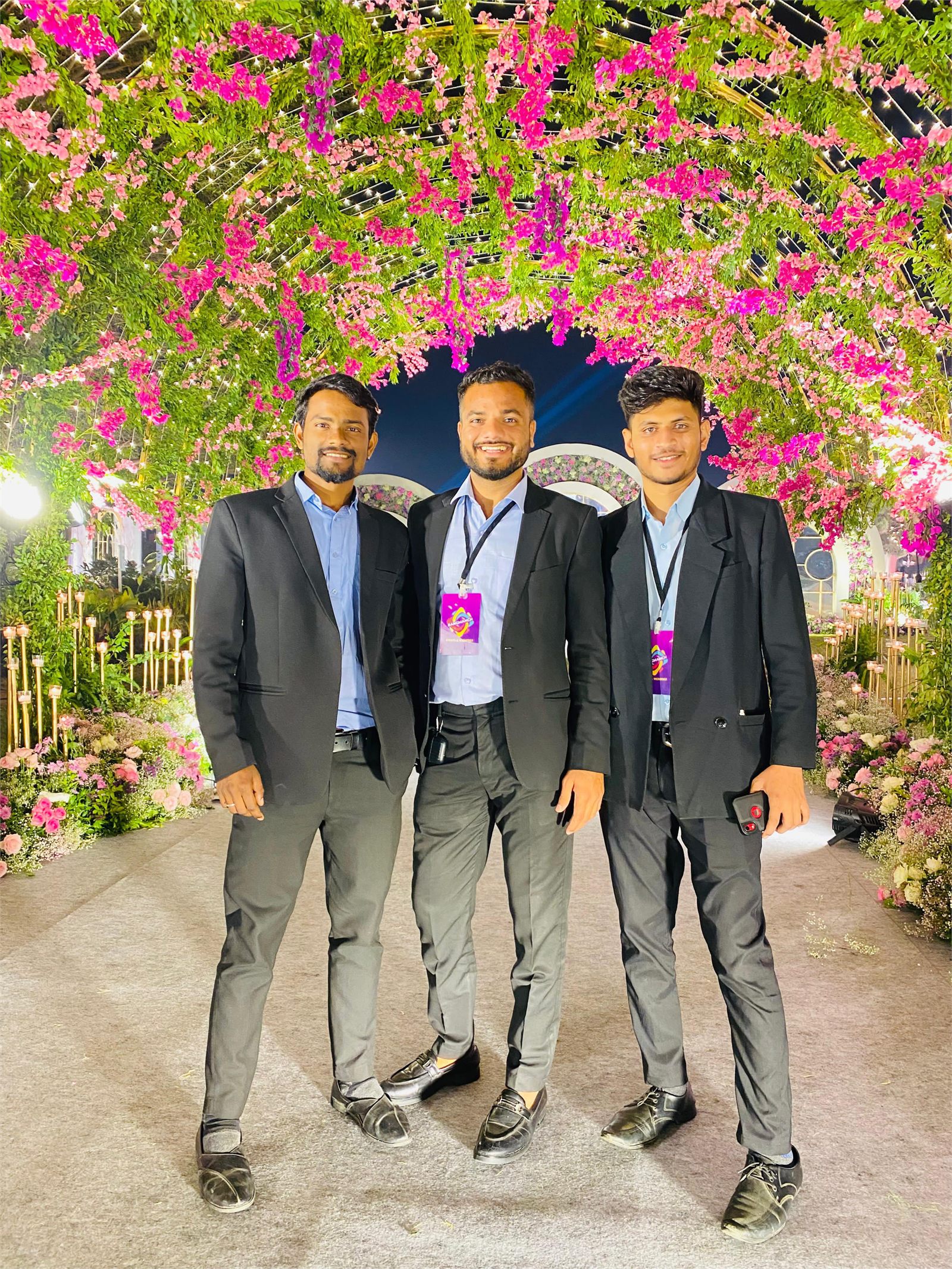 Three Indraa Events crew members beneath a pink and green floral entrance arch